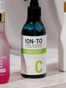 A dark blue glass pump bottle of ION-TO Hair & Scalp Science Specialist Calming Serum with a white and green label, set on a marble countertop.