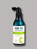 A bottle of ION-TO Hair & Scalp Calming Serum, featuring a dark teal bottle with a black spray nozzle and a white label with green text and accents, set against a solid gray background.