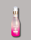 A bottle of ION-TO E Hair Essence with a pink-to-clear gradient body, a gold collar, and a clear pump dispenser, set against a solid gray background.